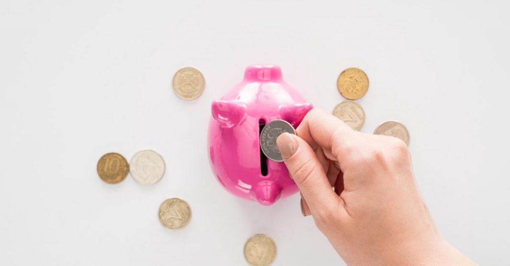 Hand with a colored nails putting coin on a piggy bank and coins