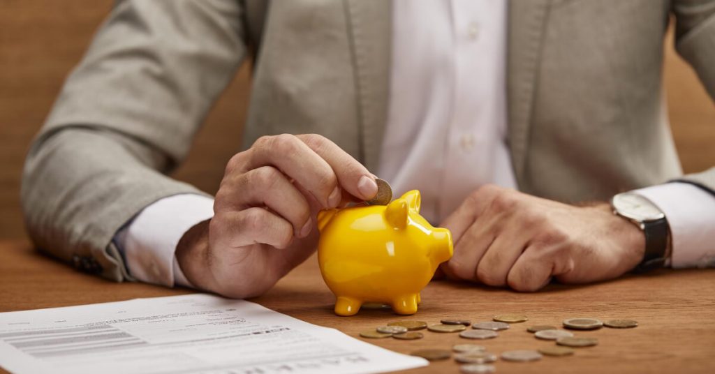 A man in a business suit that is putting a coin in a piggy bank