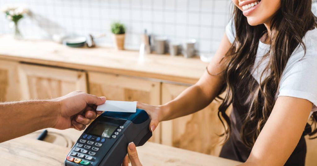 A woman who is holding a credit card machine and a man is giving her the credit card to be swipe