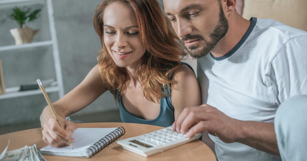 A couple that is planning to save money, the man is using a calculator while the woman is writing on the notebook