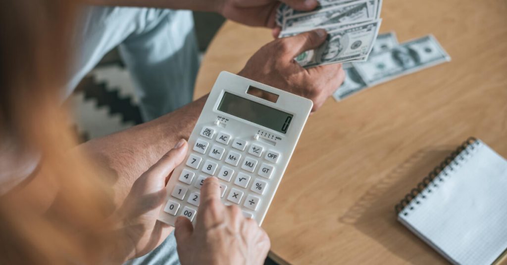 A woman holding a calculator and the man is holding dollar bills